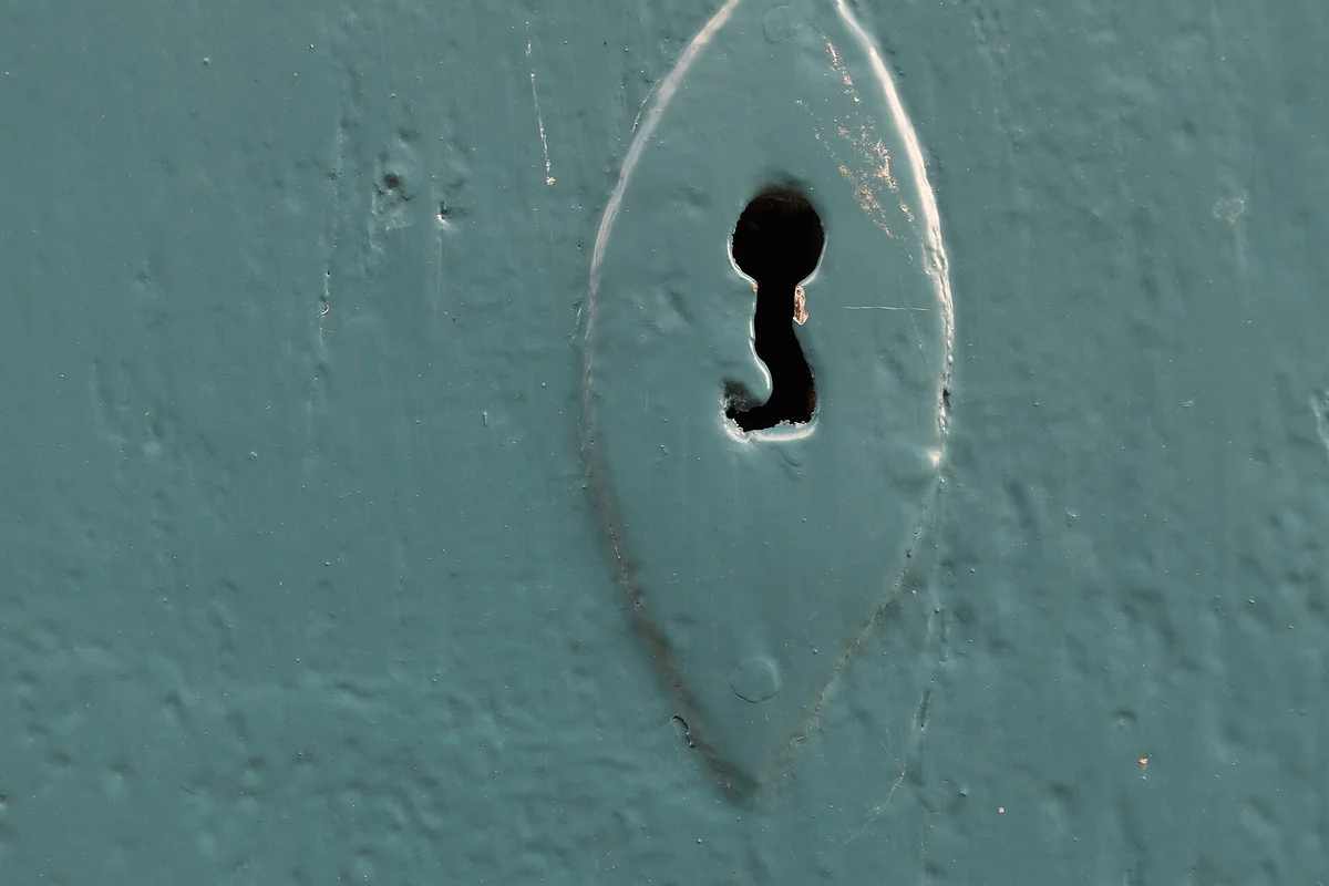 Metamour moving in: a keyhole and its escutcheon plate in a teal-painted front door