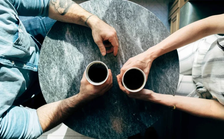 Platonic relationship: two people sitting together at a marble table with coffee, hands resting on the surface, sharing a companionable moment